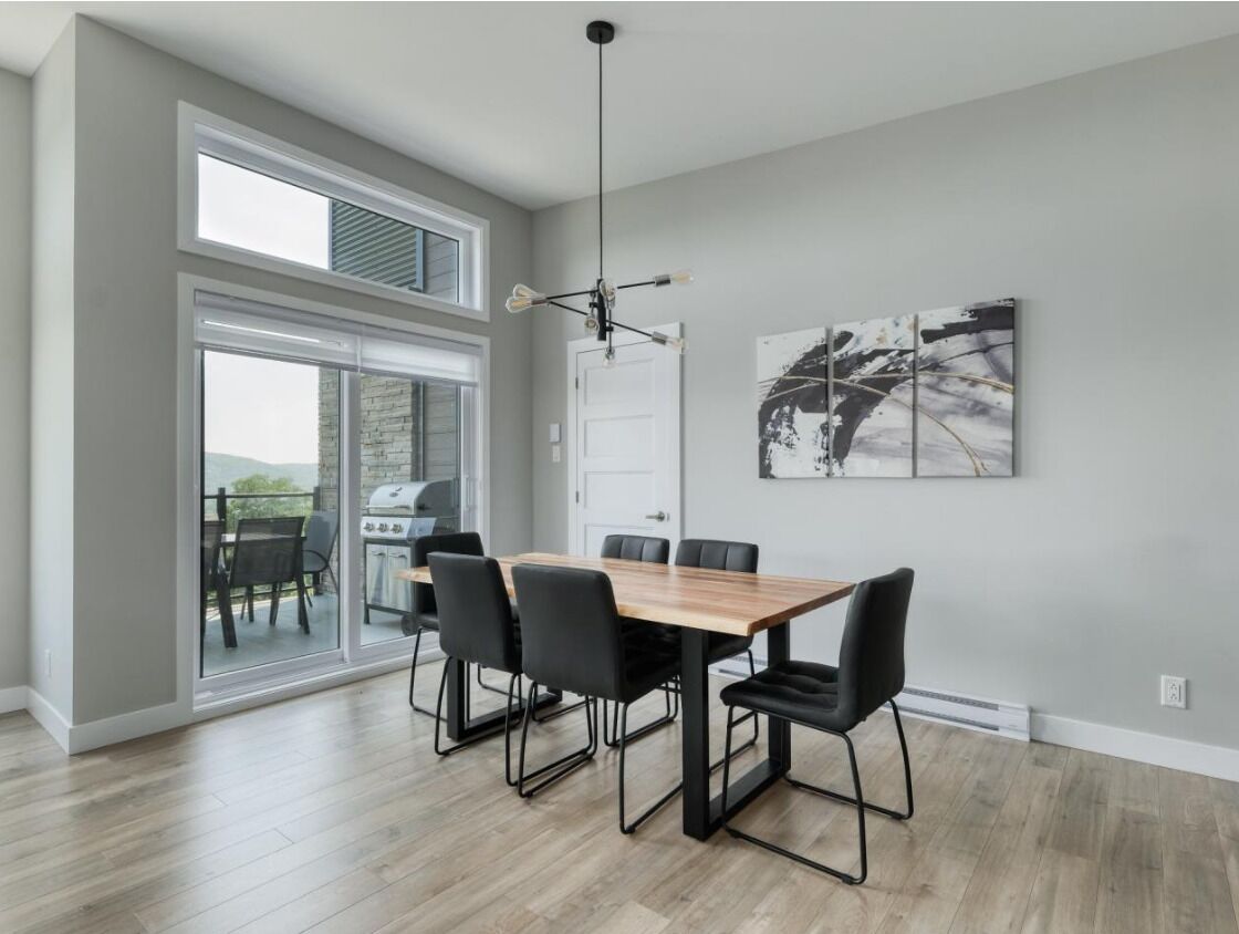 A modern dining area with a wooden table and black chairs, a large window, and a ceiling fan.