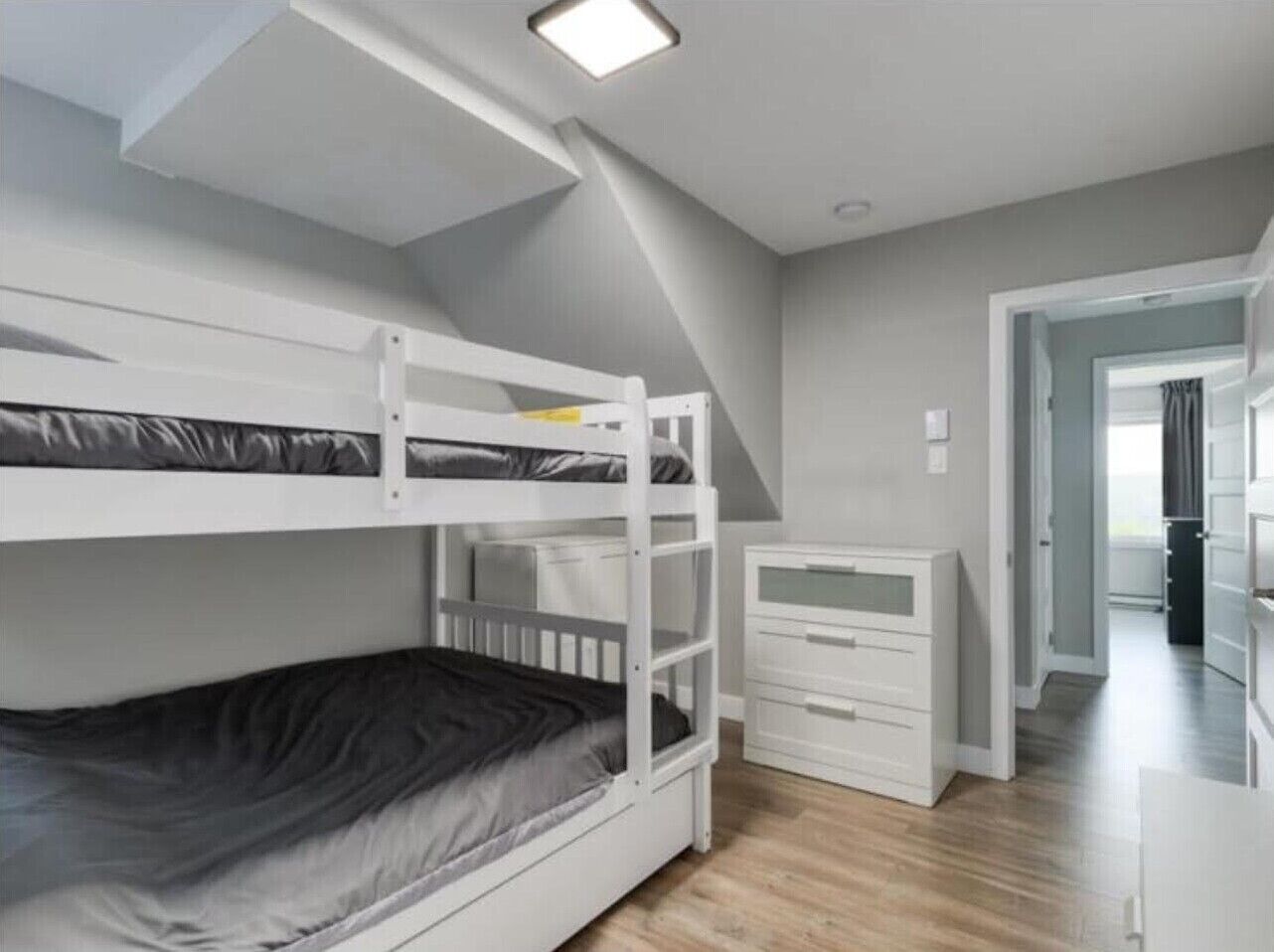 Une chambre avec un lit superposé, une commode blanche et un dressing.