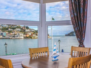 A table with chairs and a sailboat model in front of a window overlooking a coastal town. - Castleview Apartment, 21 South Embankment (Dartmouth)