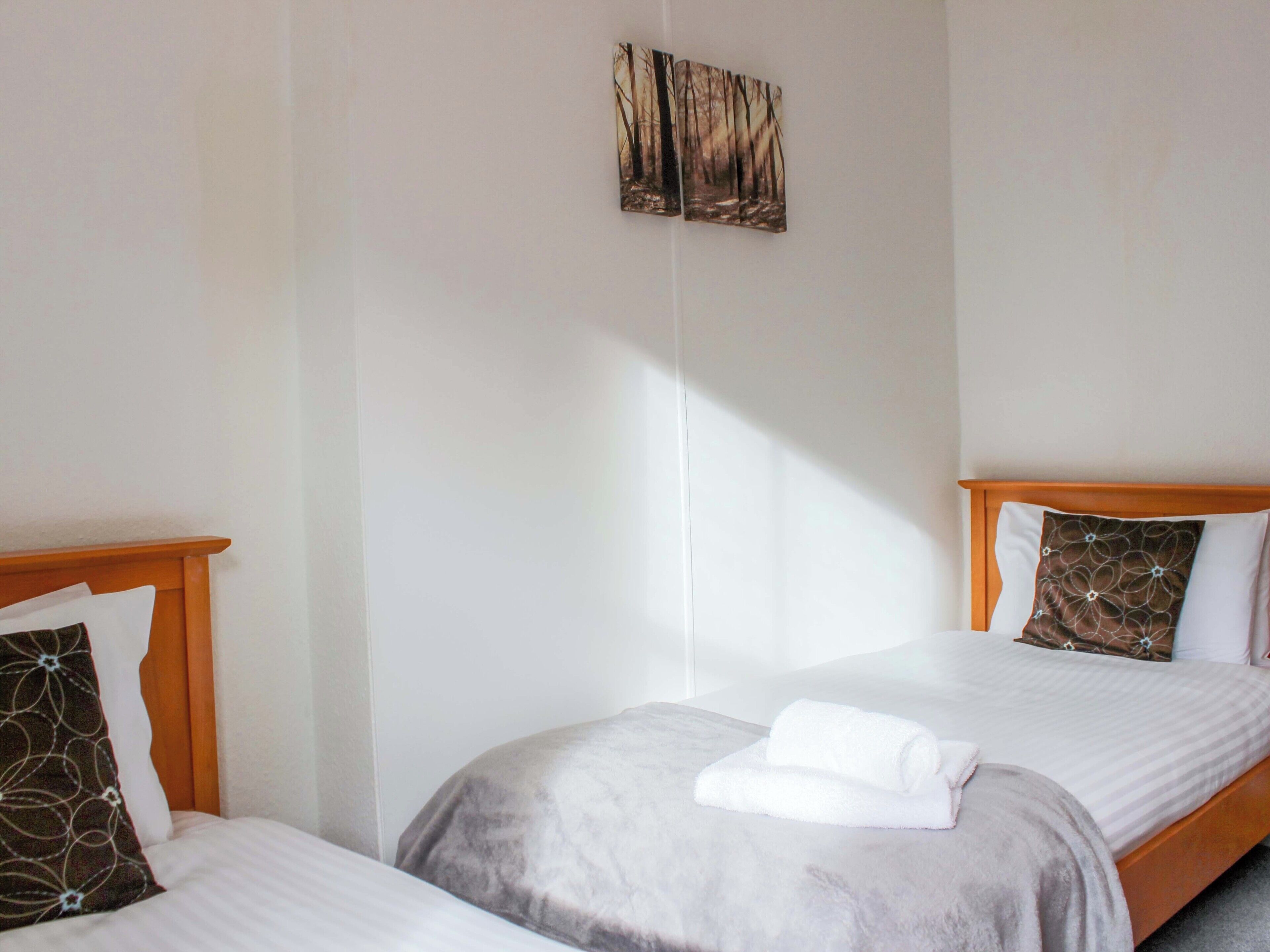 Une chambre d’hôtel avec deux lits, chacun doté d’une tête de lit en bois et d  ’un oreiller blanc. Une grande fenêtre laisse entrer la lumière naturelle dans la pièce.