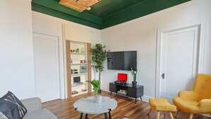 A living room with a grey sofa, a yellow armchair, a round coffee table, a black TV stand, and a bookshelf.