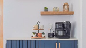 A kitchen with a blue cabinet, wooden shelves, a coffee maker, and decorative items.