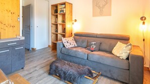 A cozy living room with a grey sofa, wooden bookshelf, and a fur-covered ottoman.