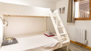 A bunk bed with a ladder, a bedside table with a pillow, a window with curtains, and a radiator.
