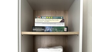 A closet with three shelves, each holding folded white towels. On the top shelf, there are books titled 'Vegan on the Go', 'Honestly Healthy for Life', and 'The Royal Horticultural Society Encyclopedia of Plants & Flowers'. - Cozy Notting Hill 1 Bedroom - Prime Spot (London)