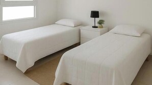 Una stanza con due letti singoli, un comodino con una lampada e una finestra che lascia entrare luce naturale.