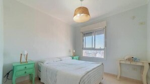 Une chambre à coucher comprenant un lit, une table de chevet, une commode, une fenêtre et un luminaire suspendu.