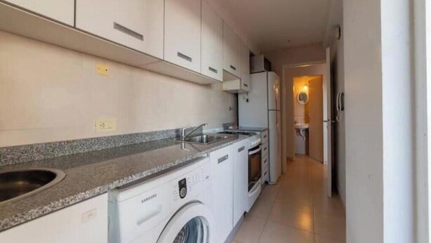 Une cuisine compacte équipée d’un lave-linge encastré, d’un évier et d’un réfrigérateur.