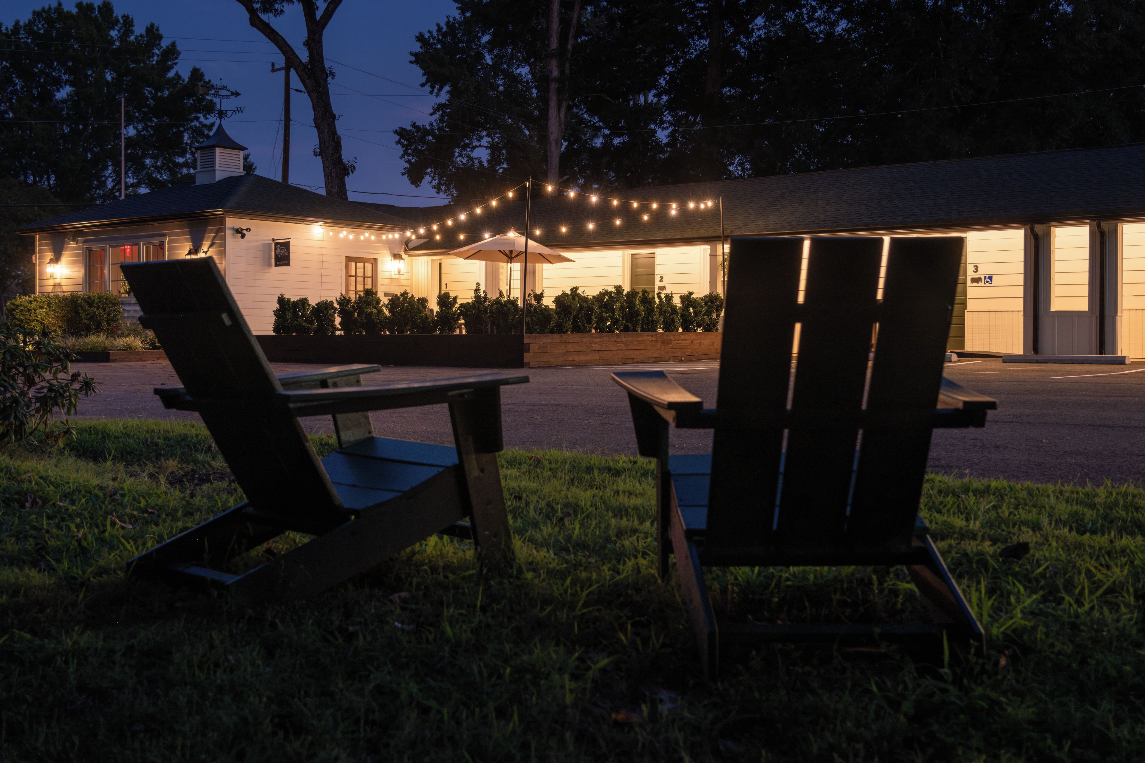 Un espacio al aire libre con dos sillas, una mesa, un edificio con porche y guirnaldas de luces.