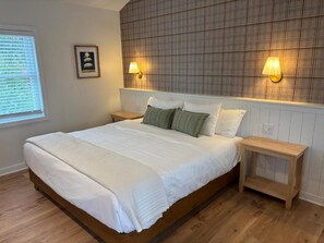 Un dormitorio con una cama grande, dos mesitas de noche, un cabecero estampado con cuadros y dos lámparas fijadas a la pared.