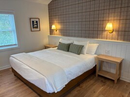 Un dormitorio con una cama grande, dos mesitas de noche, un cabecero estampado con cuadros y dos lámparas fijadas a la pared.