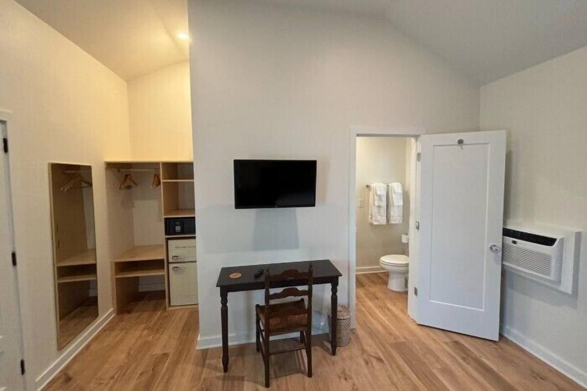 A room with a desk, chair, television, closet, and a door leading to a bathroom.