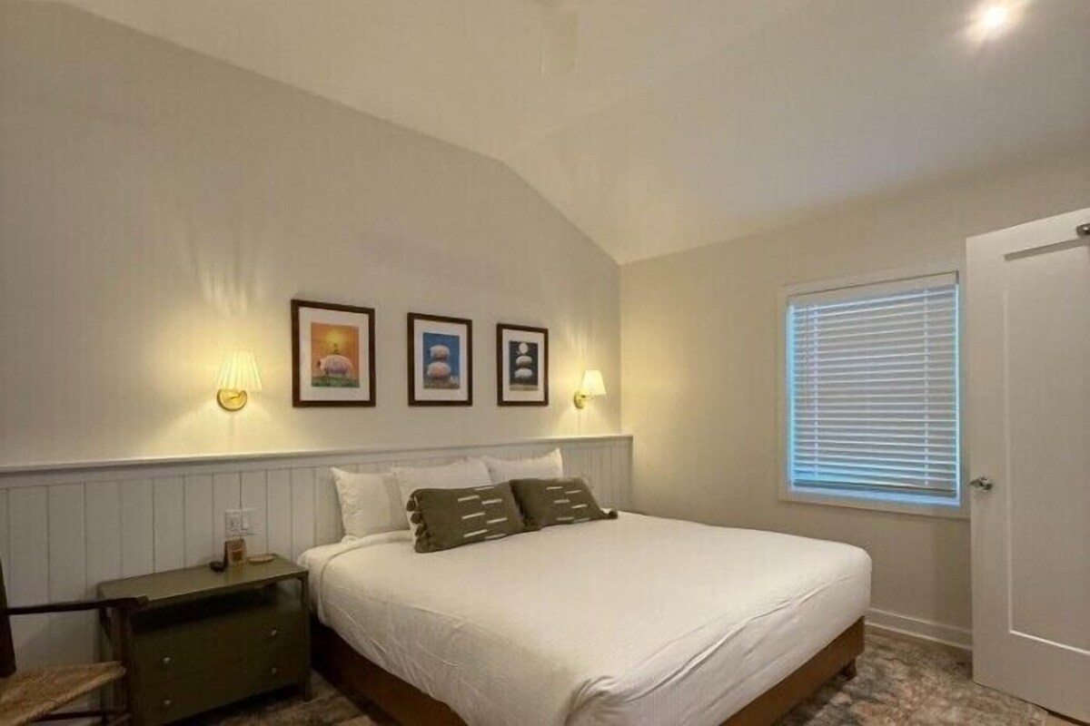 A bedroom with a bed, a nightstand, a window with blinds, and wall-mounted lights.
