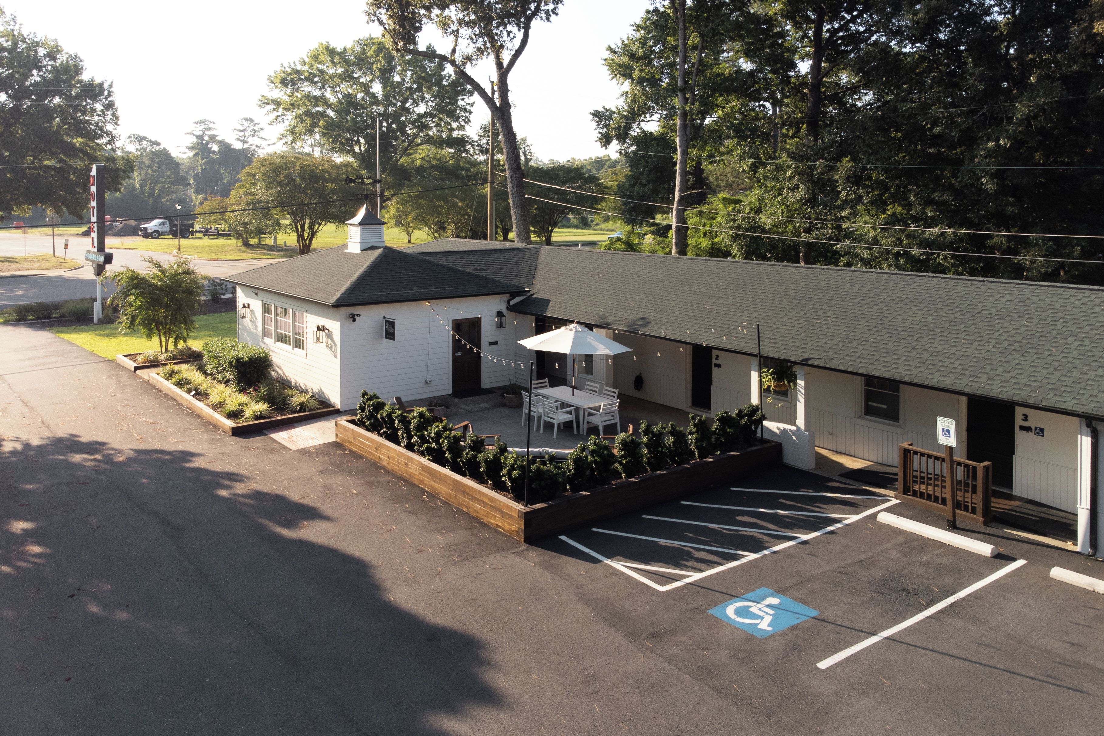 Un motel con estacionamiento, una zona de estar al aire libre cubierta y un espacio de estacionamiento accesible para discapacitados.