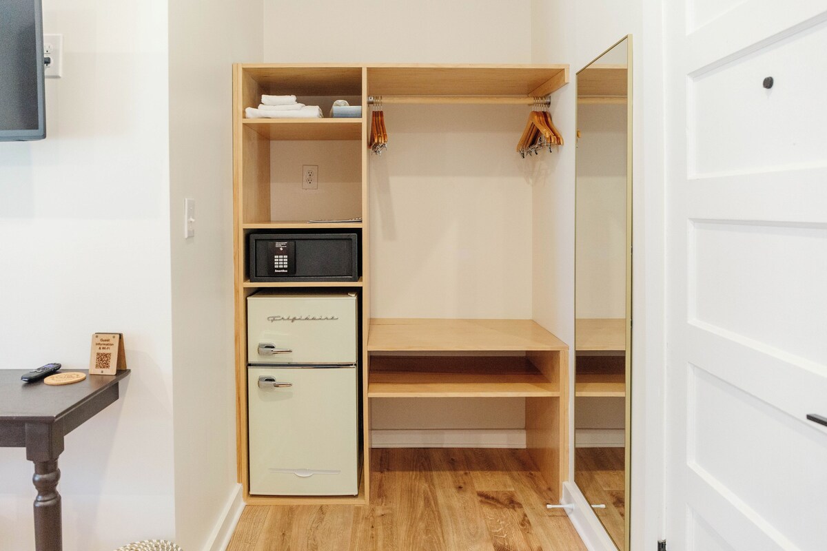 A compact room with a wooden wardrobe, a white refrigerator, and a small table with a remote control.