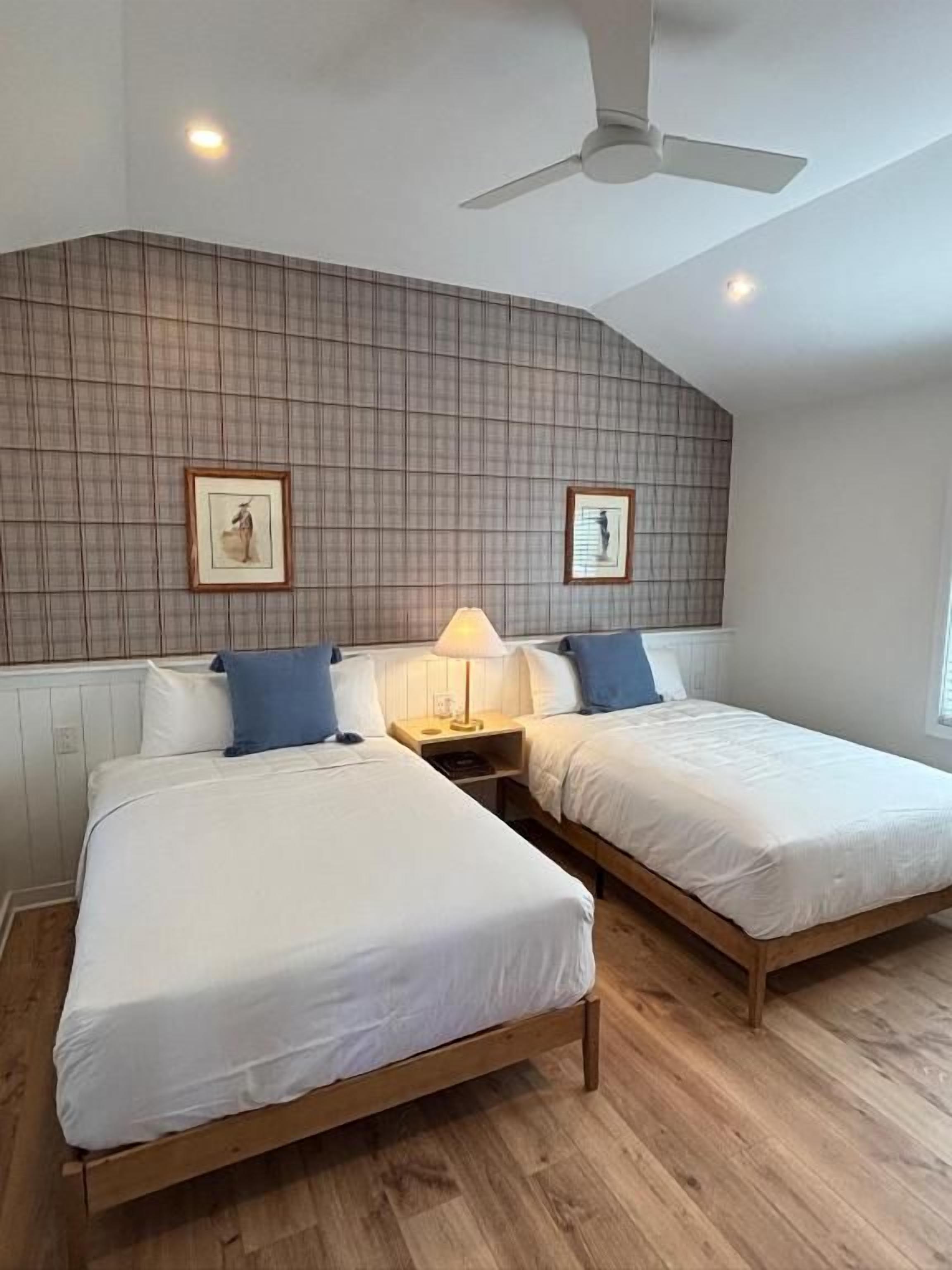 A room with two beds, a ceiling fan, and framed pictures on the wall.