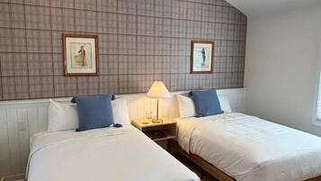 A room with two beds, a ceiling fan, and framed pictures on the wall.