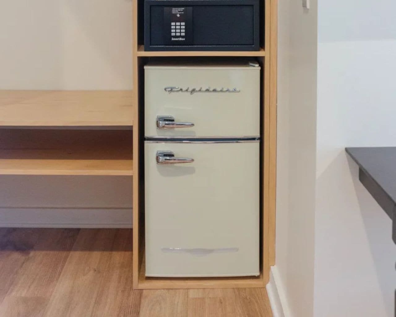A compact refrigerator with a control panel on top, situated in a kitchen with wooden cabinetry and a countertop.