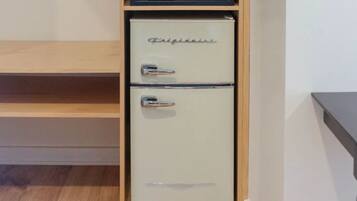 A compact refrigerator with a control panel on top, situated in a kitchen with wooden cabinetry and a countertop.