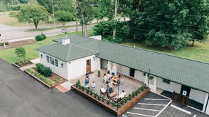 A white building with a green roof, a covered patio with outdoor seating, and a parking lot. - Rochambeau Roadside Inn (Williamsburg)