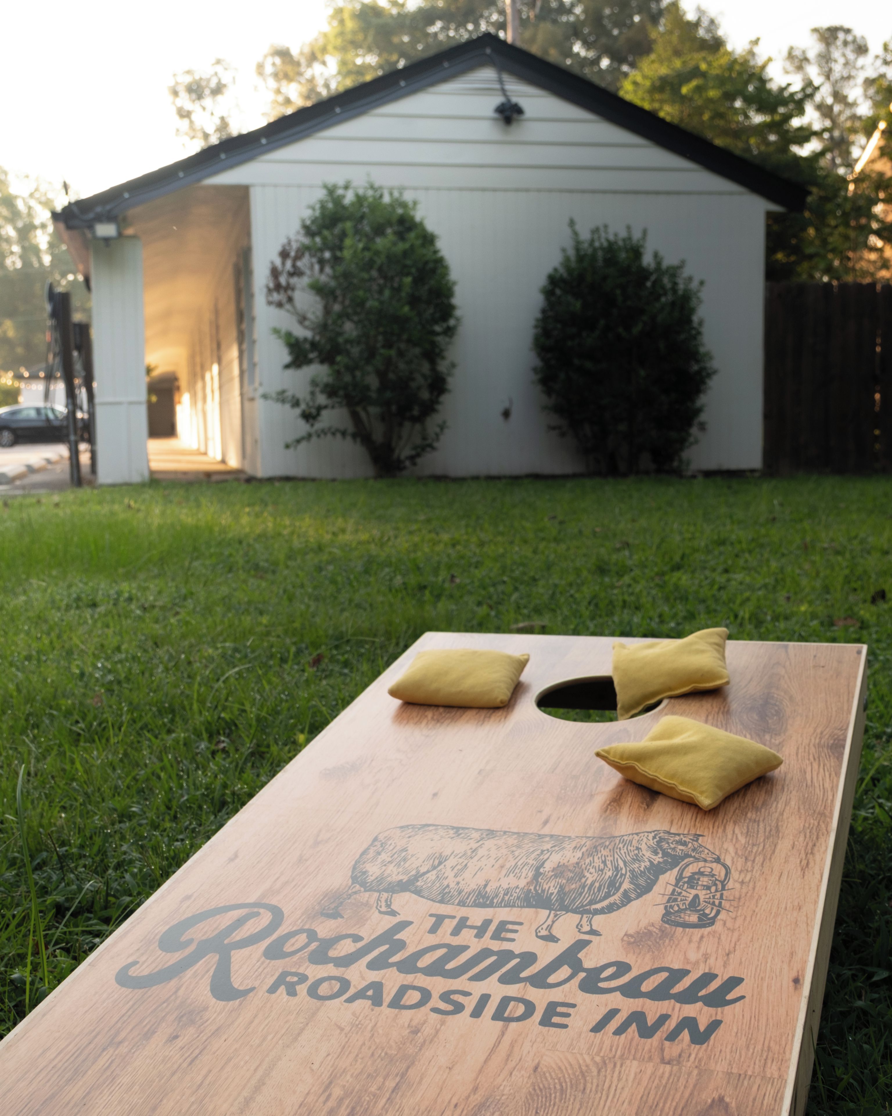 A wooden board with 'The Rockamabe Roadside Inn' text and a logo, placed on grass with two cushions on it.