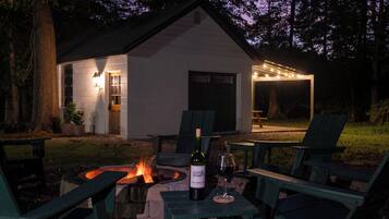Un área de estar al aire libre acogedora, con un brasero, una mesa y una botella de vino, además de sillas.
