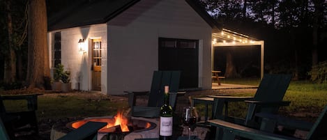 Un espace extérieur accueillant avec des sièges confortables, un foyer, une table avec une bouteille de vin et des chaises.