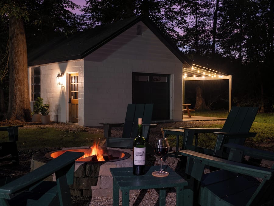 A cozy outdoor seating area with a fire pit, a table with a bottle of wine, and chairs.