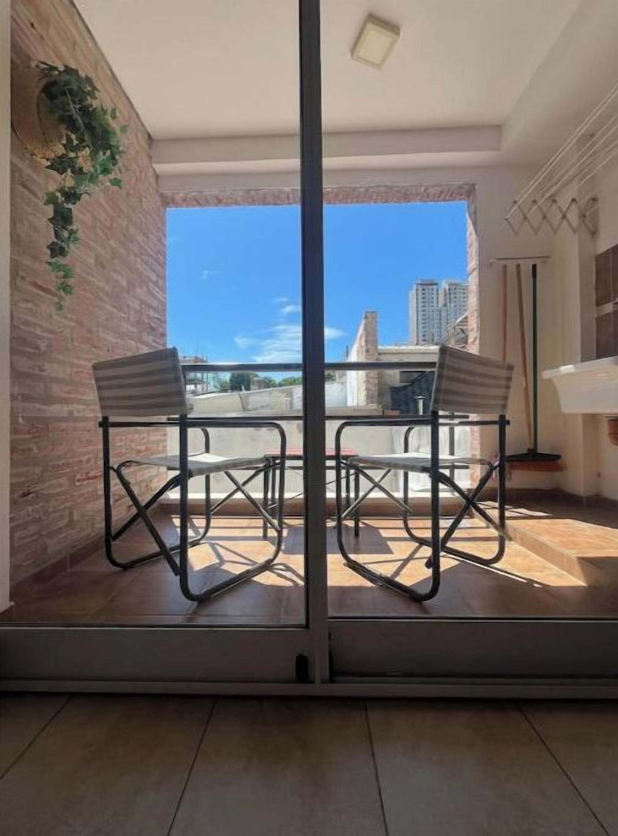 Un balcón con mesa y sillas, un muro de ladrillo y vistas a edificios.