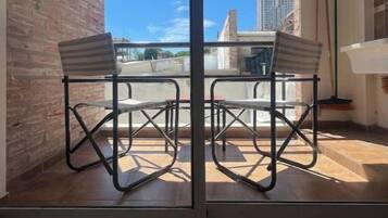 Un balcón con mesa y sillas, un muro de ladrillo y vistas a edificios.