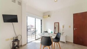 Una habitación moderna con una mesa redonda, dos sillas negras, un televisor de pantalla plana montado en la pared y un ventanal corredero que da a un espacio exterior.