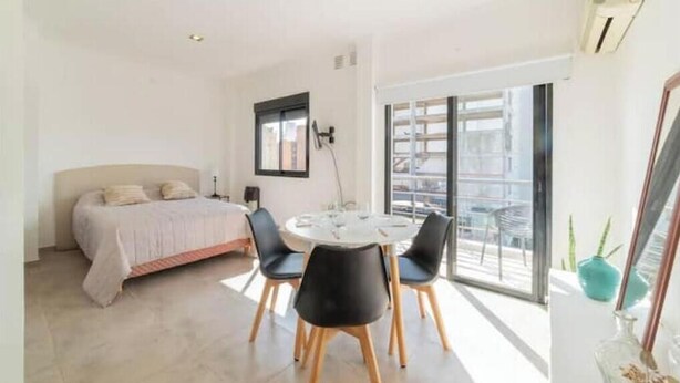 Un dormitorio con cama, una mesa de comedor con sillas, una ventana y un balcón.