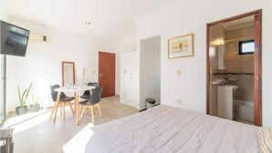 Un dormitorio con una cama grande, un escritorio con sillas, un televisor y un baño visible a través de una puerta abierta.