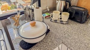 Una cocina con tetera, tostadora, dos tazas, una olla y utensilios sobre la encimera.