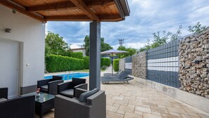 A covered outdoor area with wicker furniture, a swimming pool, and a stone wall.