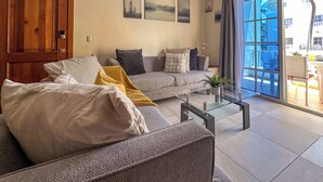 A modern living room with a grey sofa, a coffee table, and a large sliding glass door leading to an outdoor area.