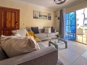 Una sala de estar moderna con un sofá gris, una mesa de centro y un amplio ventanal corredizo que da a un espacio exterior.