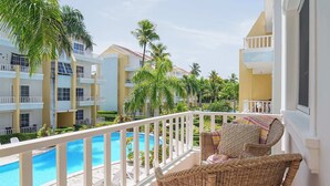 A balcony with wicker chairs, a pool, and a view of a resort building.