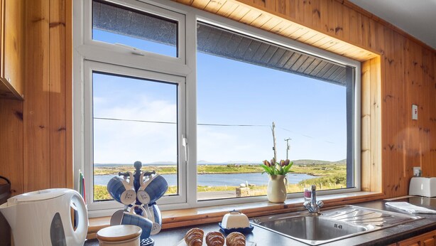 Una cocina con armarios de madera, un ventanal con vistas a un lago, una tetera, una taza y croissants sobre la encimera.