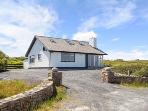 A single-story house with a sloped roof, a stone wall entrance, and a gravel driveway.
