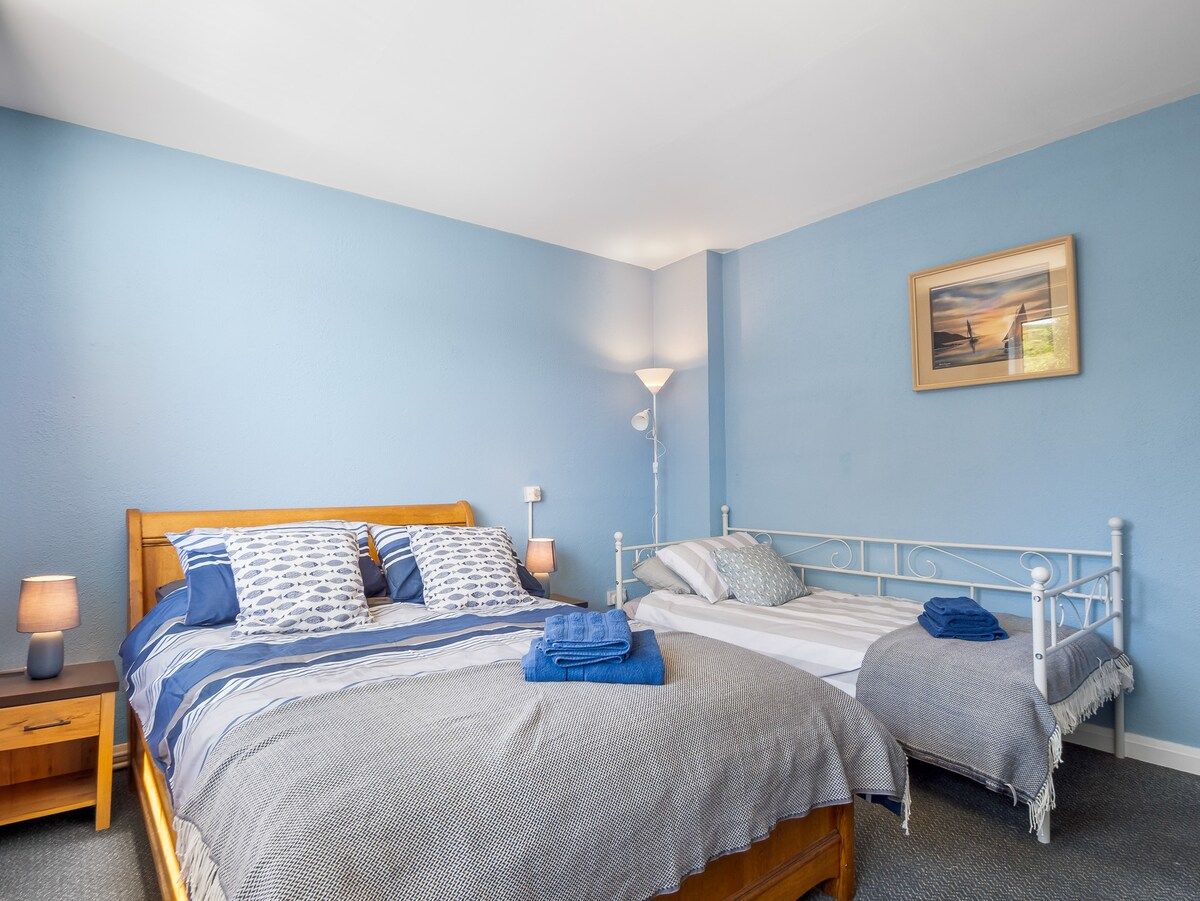A bedroom with two beds, a nightstand, a lamp, and a painting on the wall.