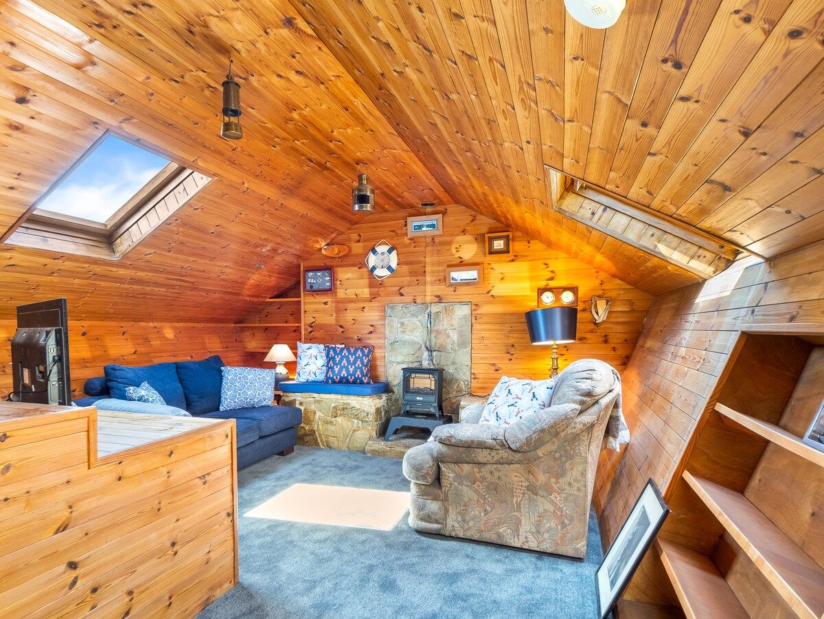 A cozy cabin interior with a stone fireplace, wooden walls, a sofa, and a small table.