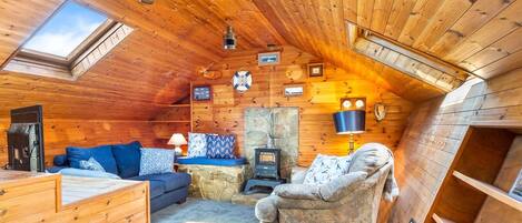 A cozy cabin interior with a stone fireplace, wooden walls, a sofa, and a small table.