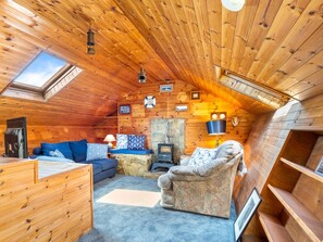 Un acogedor interior de cabaña con chimenea de piedra, paredes de madera, un sofá y una pequeña mesa.
