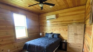 A wooden cabin bedroom with a bed, a ceiling fan, a window, and a wardrobe. - The Bear Den ATV friendly (Mena)