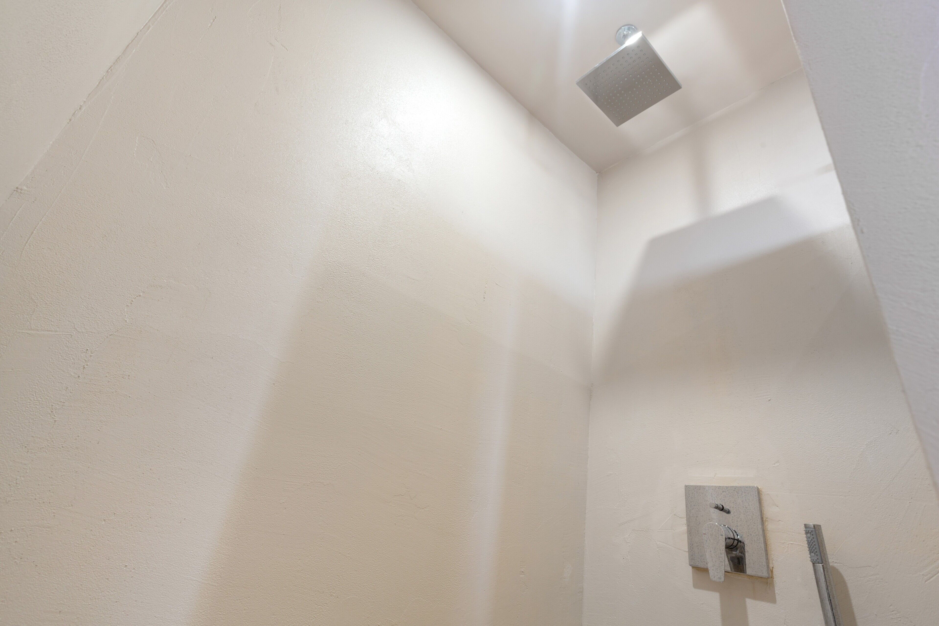 A corner of a room with a white wall, a light fixture, and a shower control panel.
