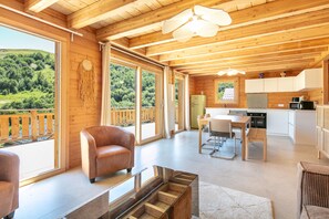 Een houten chalet met een eethoek, keuken en grote ramen met uitzicht op een bebost gebied.