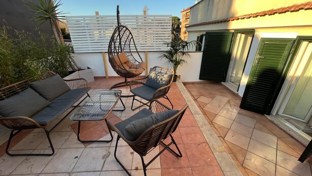 An outdoor patio with wicker furniture, a hanging chair, and a glass table. - Testaccio Terrace (Roma)