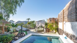 A swimming pool with a stone border, a thatched-roof structure, and a white building with a wooden fence. - Villa Oceania Entire with Sea View, Wi-Fi and Air Conditioning (Chayofa)