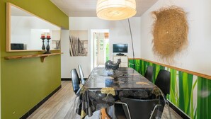 A dining area with a long table, chairs, a hanging light fixture, a mirror, and a wall-mounted decorative item. - Holiday Home 'Du Porche' with Private Terrace and Wi-Fi (Chaillevette)